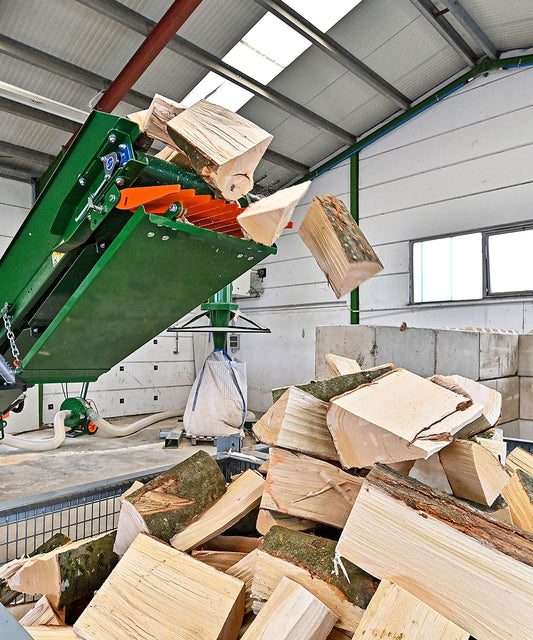 Frisch gespaltenes Brennholz fällt aus einer automatisierten Maschine in einer modernen Halle in einen Gitterbehälter.